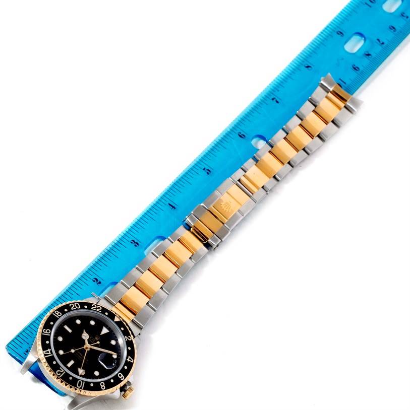 The Rolex GMT-Master 16713 Men
s Stainless Steel Black Dial 16713 Men
s Stainless Steel Black Dial watch is shown flat with its face and bracelet fully visible, alongside a blue ruler for scale.