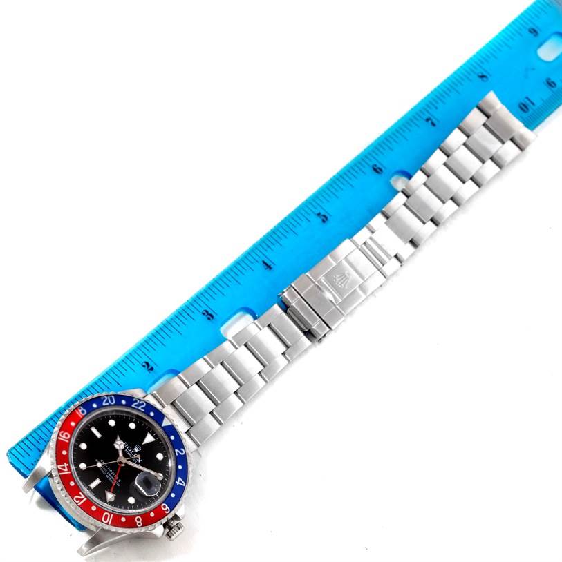 The image shows a Rolex GMT-Master 16710 Men's Stainless Steel Black Dial 16710 Men's Stainless Steel Black Dial watch laid flat, with a blue ruler measuring the metal bracelet.