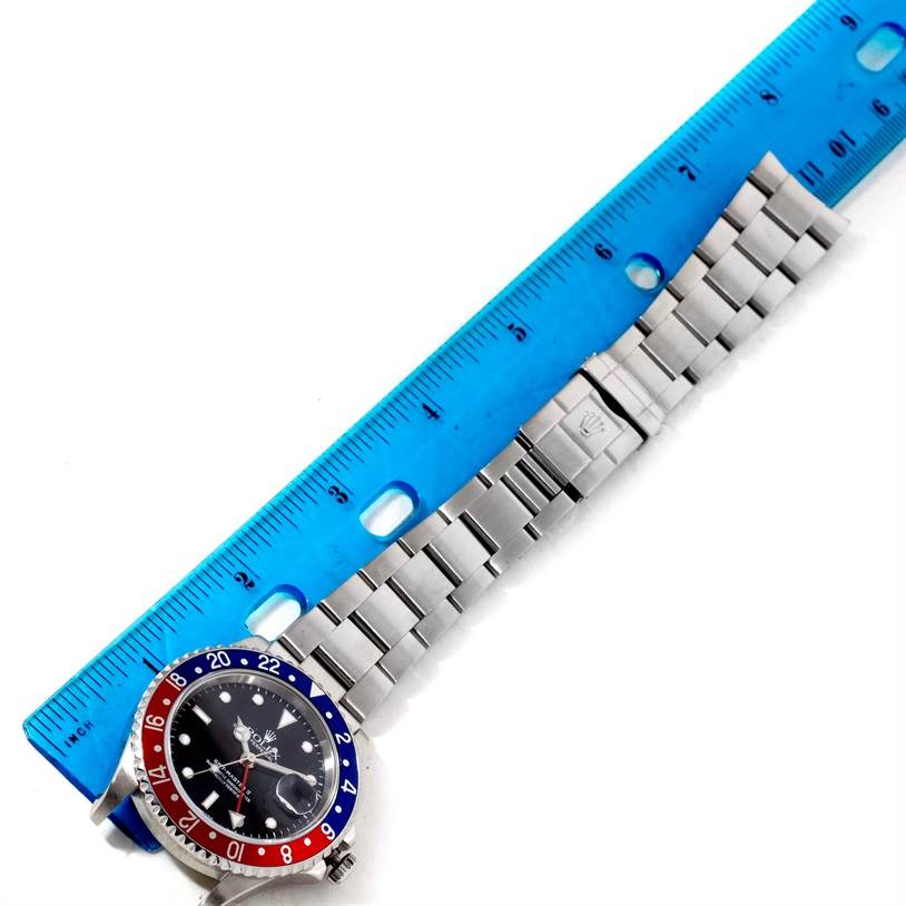 The image shows a top view of a Rolex GMT-Master 16710 Men's Stainless Steel Black Dial 16710 Men's Stainless Steel Black Dial watch with a blue and red bezel, next to a blue ruler.