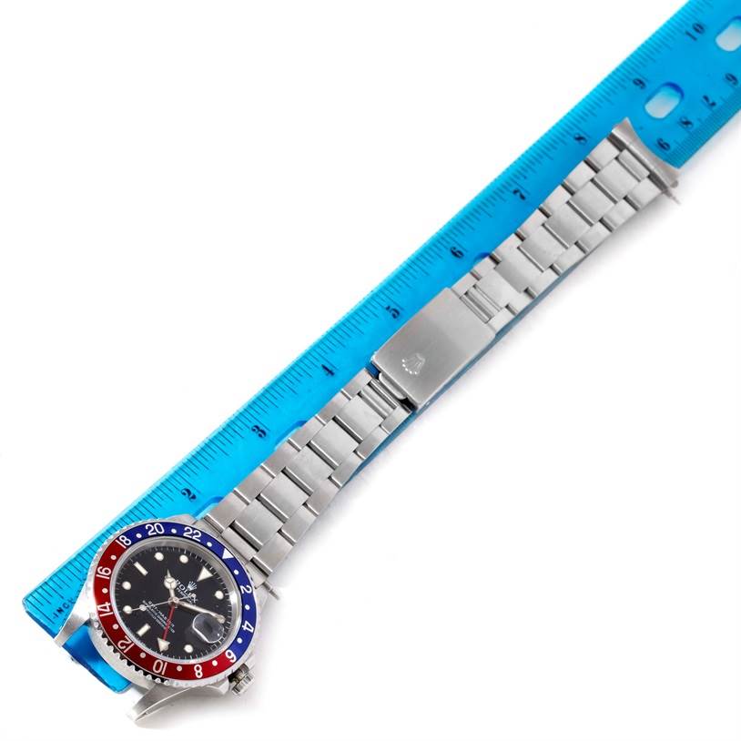 The image shows a Rolex GMT-Master 16700 Men's Stainless Steel Black Dial 16700 Men's Stainless Steel Black Dial watch laid flat with a blue ruler for size reference, highlighting the face, bezel, and stainless steel bracelet.