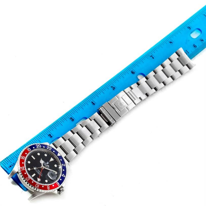 This image shows a top view of a Rolex GMT-Master 16710 Men's Stainless Steel Black Dial 16710 Men's Stainless Steel Black Dial watch with a stainless steel bracelet and multicolor bezel beside a blue ruler.