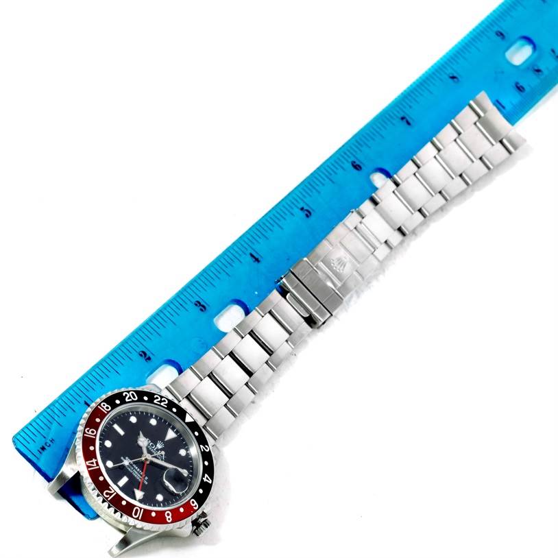 The Rolex GMT-Master 16710 Men's Stainless Steel Black Dial 16710 Men's Stainless Steel Black Dial watch is shown horizontally with a metal strap and bezel, alongside a blue ruler for measurement.