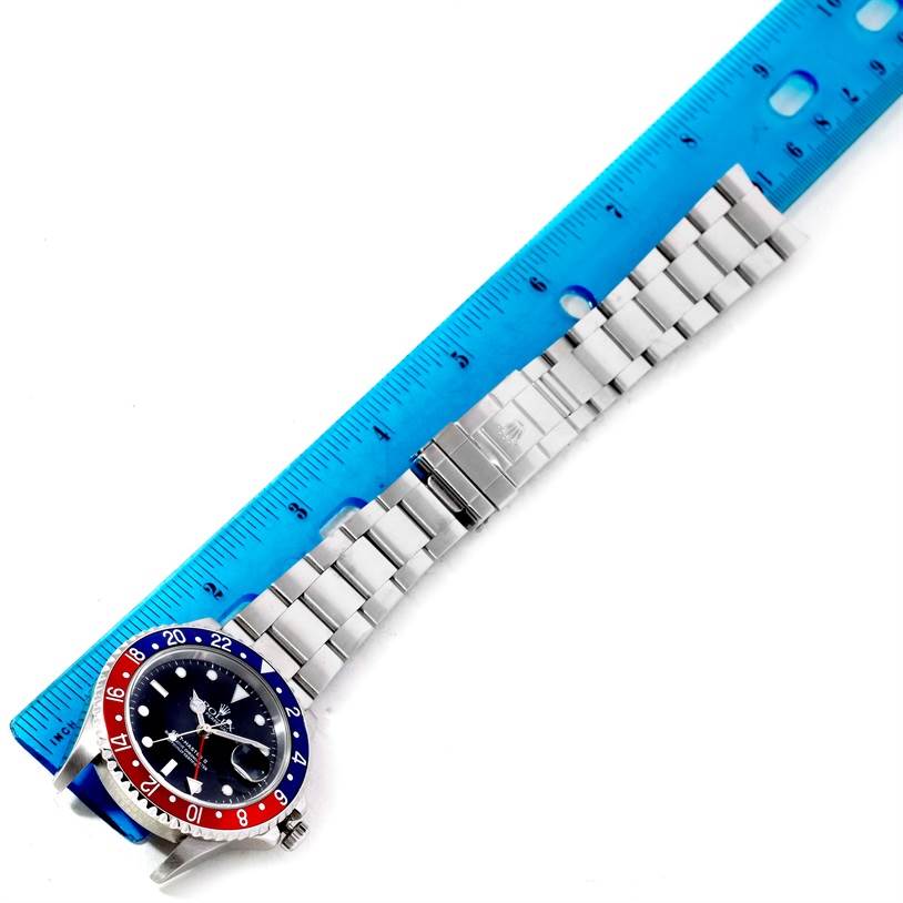 The image shows a top-down view of a Rolex GMT-Master 16710 Men's Stainless Steel Black Dial 16710 Men's Stainless Steel Black Dial watch with its stainless steel bracelet extended alongside a blue ruler.