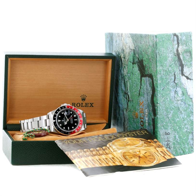 The Rolex GMT-Master 16710 Men's Stainless Steel Black Dial 16710 Men's Stainless Steel Black Dial watch is displayed in its green and wood box, alongside its booklet and a green tag.