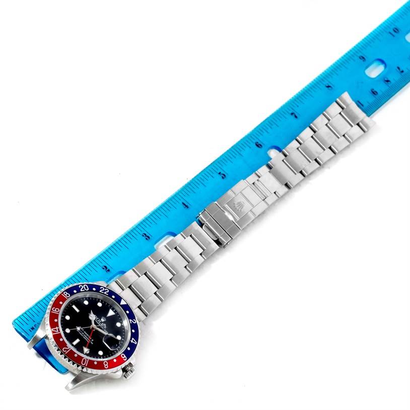 The image shows a Rolex GMT-Master 16710 Men's Stainless Steel Black Dial 16710 Men's Stainless Steel Black Dial watch laid flat with its bezel, dial, and bracelet visible, alongside a blue ruler for measurement.