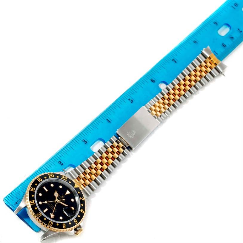 The image shows a Rolex GMT-Master 16713 Men
s Stainless Steel Black Dial 16713 Men
s Stainless Steel Black Dial watch with a jubilee bracelet beside a blue ruler from a top-down angle.