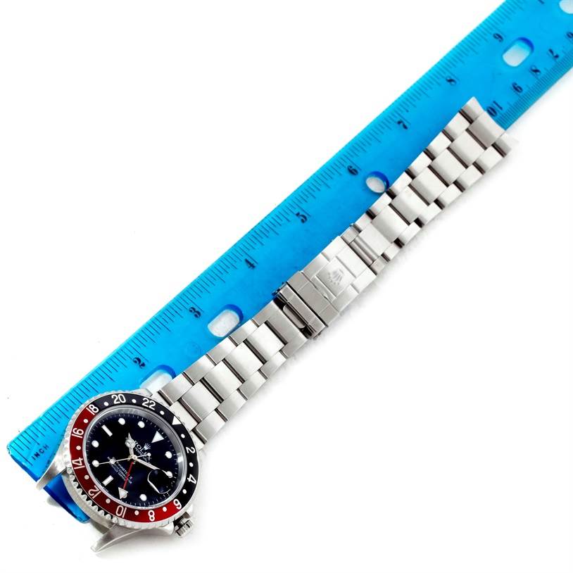 The image shows a Rolex GMT-Master 16710 Men's Stainless Steel Black Dial 16710 Men's Stainless Steel Black Dial watch laid horizontally next to a blue ruler, displaying the watch face and stainless steel bracelet.