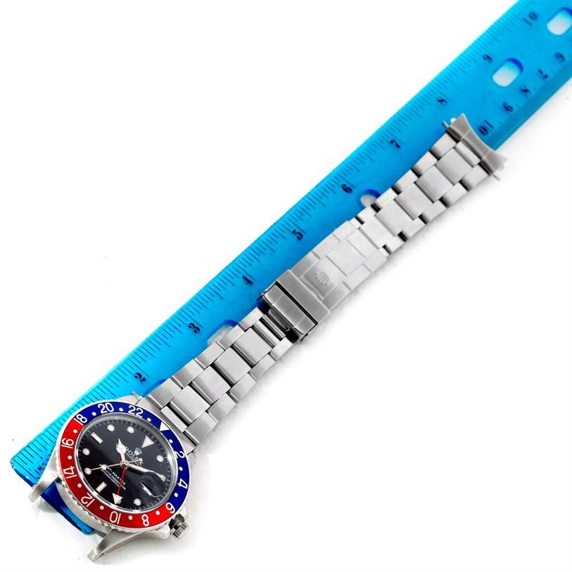 The image shows a Rolex GMT-Master 16750 Men's Stainless Steel Black Dial 16750 Men's Stainless Steel Black Dial watch laid flat next to a blue ruler, showcasing its dial, bezel, and metal bracelet.