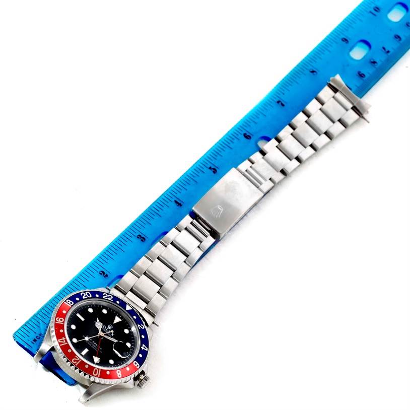 The Rolex GMT-Master 16700 Men
s Stainless Steel Black Dial 16700 Men
s Stainless Steel Black Dial watch is shown laid flat with a blue ruler for scale, displaying its bezel, dial, and bracelet.