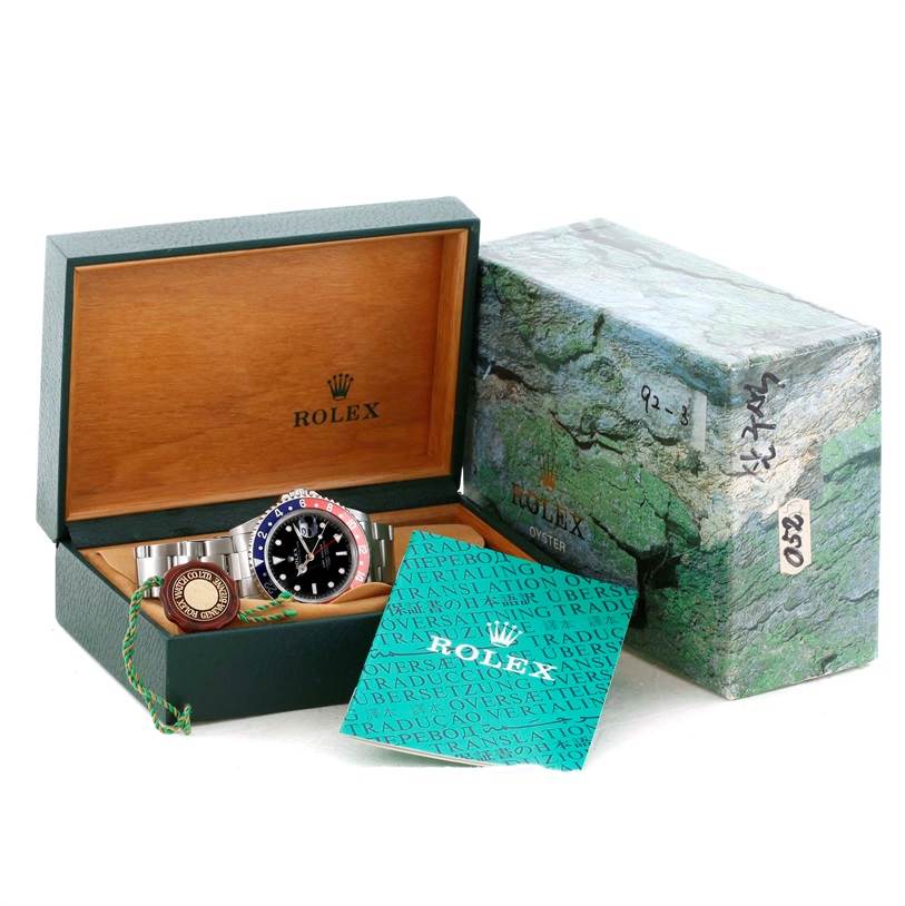 The image shows a Rolex GMT-Master 16700 Men
s Stainless Steel Black Dial 16700 Men
s Stainless Steel Black Dial watch in its open green and wood box with accompanying booklets and tags.
