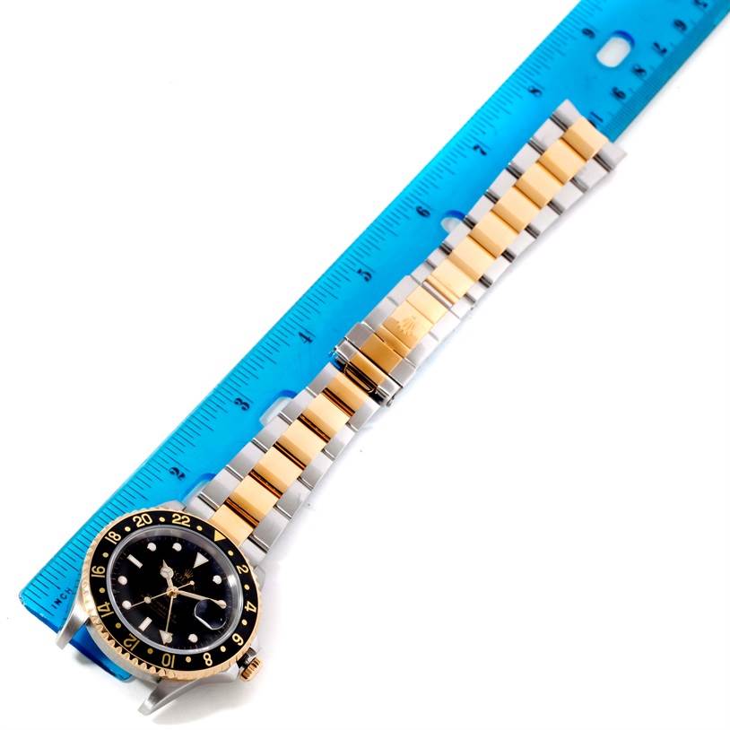 The image shows a Rolex GMT-Master 16713 Men's Stainless Steel Black Dial 16713 Men's Stainless Steel Black Dial watch with a black dial and two-tone bracelet, placed beside a blue ruler.