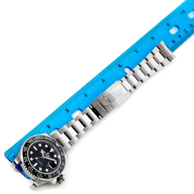 This top-down view of a Rolex GMT-Master 116710 Men's Stainless Steel Black Dial 116710 Men's Stainless Steel Black Dial watch shows the watch dial, bezel, and the entire bracelet placed next to a blue ruler.