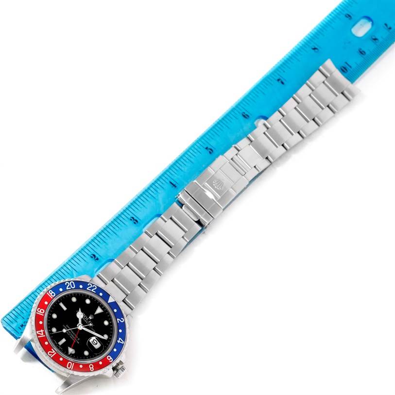 The Rolex GMT-Master 16710 Men's Stainless Steel Black Dial 16710 Men's Stainless Steel Black Dial watch is shown from a top-down angle, displaying the face, bezel, and bracelet alongside a blue ruler for scale.