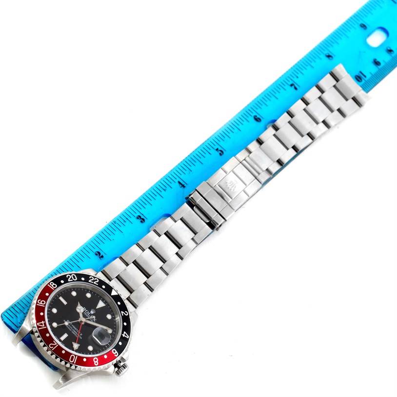 This image shows the entirety of a Rolex GMT-Master 16710 Men's Stainless Steel Black Dial 16710 Men's Stainless Steel Black Dial watch laid flat next to a blue ruler.