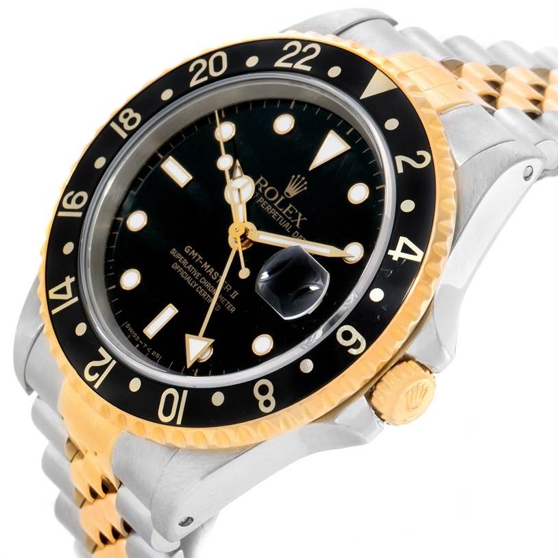 The image shows a Rolex GMT-Master 16713 Men
s Stainless Steel Black Dial 16713 Men
s Stainless Steel Black Dial II watch at an angle, highlighting the dial, black and gold bezel, and part of the bracelet.