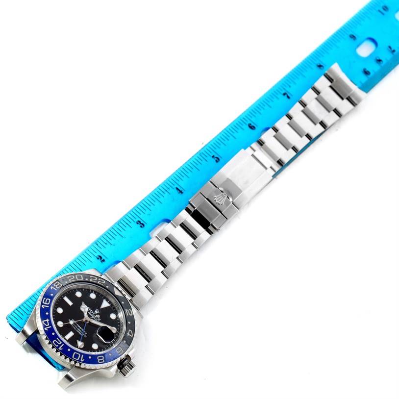 The Rolex GMT-Master 116710BLNR Men's Stainless Steel Black Dial 116710BLNR Men's Stainless Steel Black Dial watch is shown from a top-down angle, including its bracelet and part of a blue ruler.