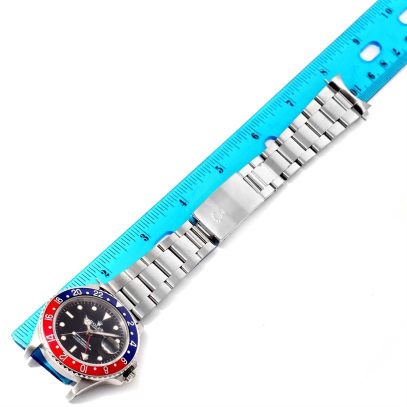 An overhead view of a Rolex GMT-Master 16700 Men's Stainless Steel Black Dial 16700 Men's Stainless Steel Black Dial watch showing the face, bezel, and metal bracelet next to a blue ruler.