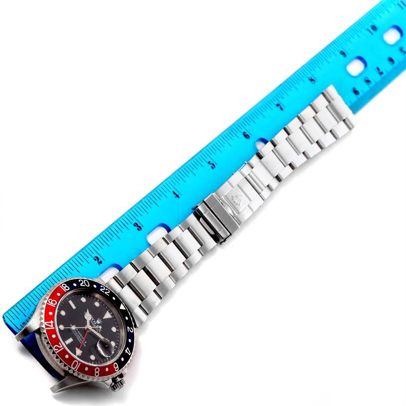 The Rolex GMT-Master 16710 Men's Stainless Steel Black Dial 16710 Men's Stainless Steel Black Dial watch is shown lying flat with a blue ruler placed alongside its bracelet for measurement.