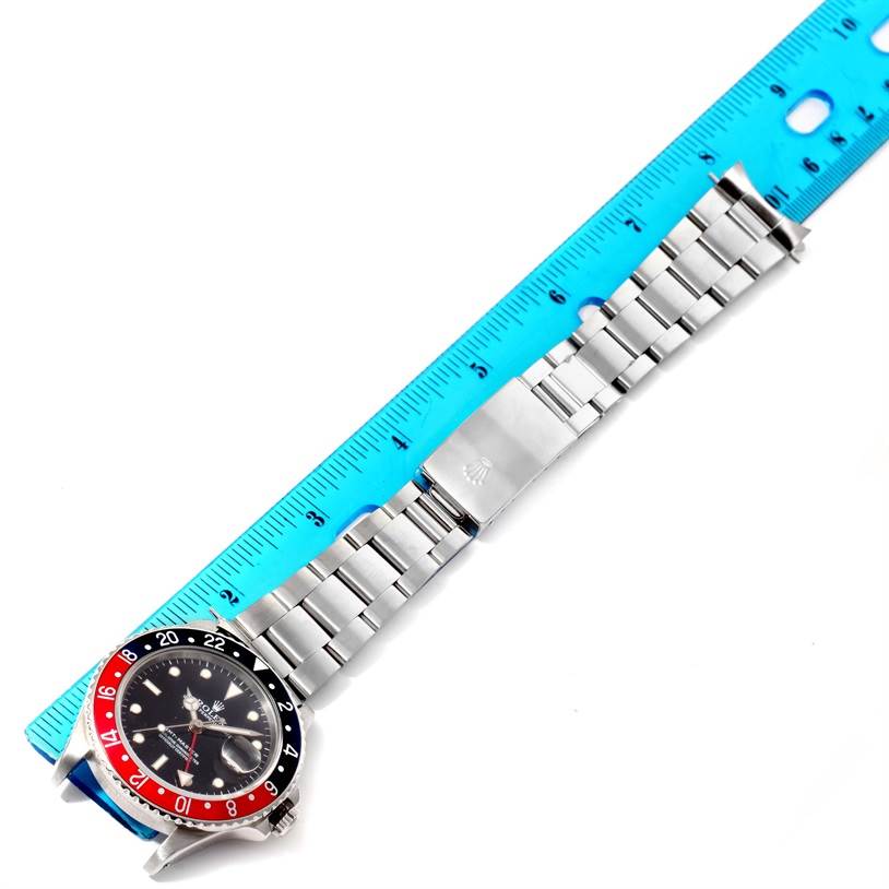 The Rolex GMT-Master 16700 Men's Stainless Steel Black Dial 16700 Men's Stainless Steel Black Dial watch is shown from a top view, displaying the watch face, bezel, and entire metal bracelet next to a ruler.