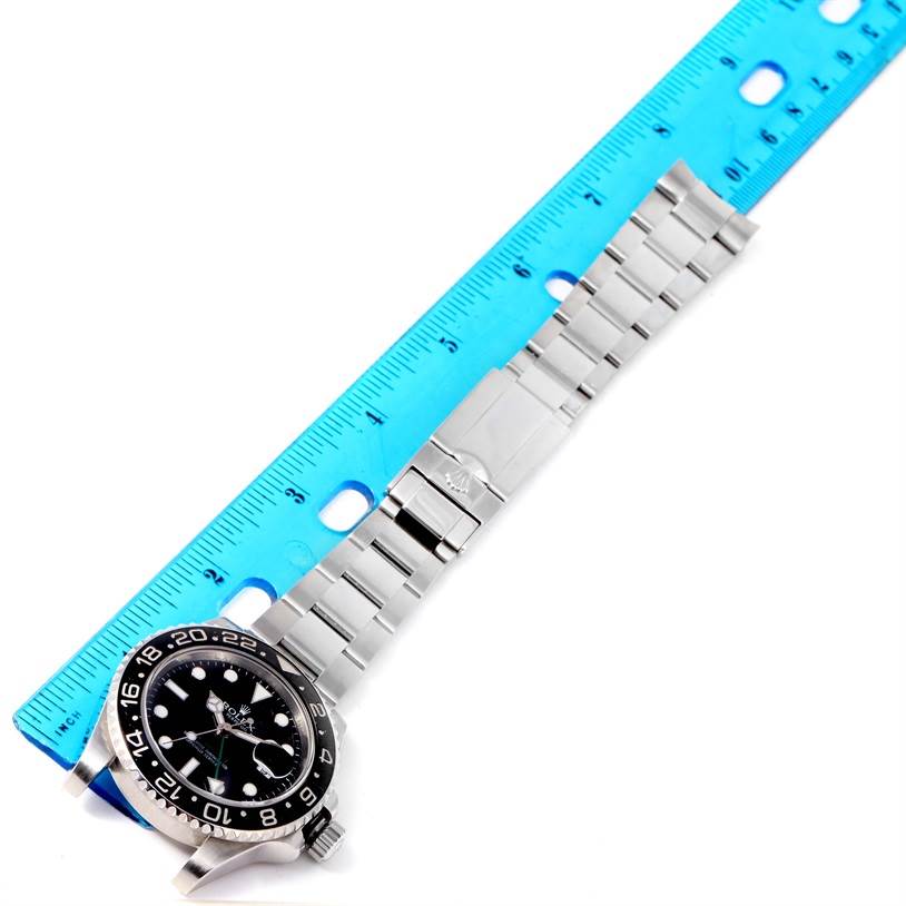 This image shows a Rolex GMT-Master 116710 Men
s Stainless Steel Black Dial 116710 Men
s Stainless Steel Black Dial watch placed alongside a blue ruler, displaying the face, bezel, and stainless steel bracelet.