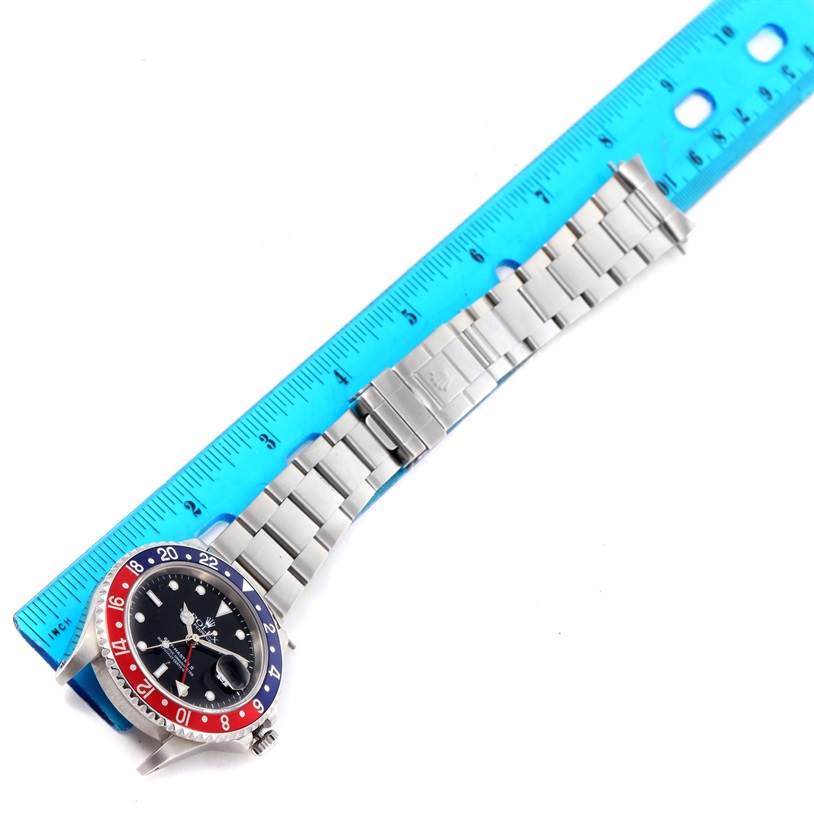 This image shows the face and bracelet of a Rolex GMT-Master 16710 Men's Stainless Steel Black Dial 16710 Men's Stainless Steel Black Dial watch, aligned with a blue inch ruler.