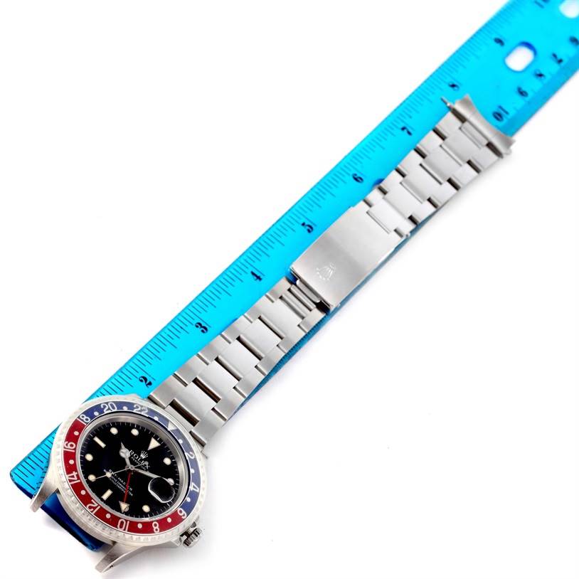 The Rolex GMT-Master 16700 Men's Stainless Steel Black Dial 16700 Men's Stainless Steel Black Dial watch is shown from above, displaying its dial, bezel, and bracelet next to a blue ruler for scale.