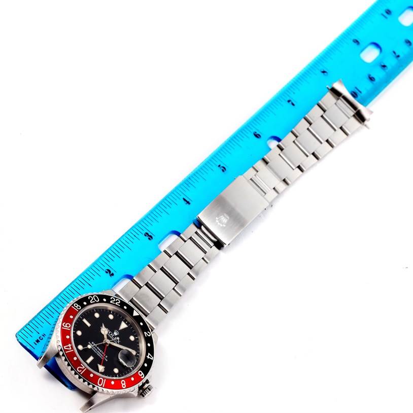 The image shows a Rolex GMT-Master 16710 Men's Stainless Steel Black Dial 16710 Men's Stainless Steel Black Dial watch laid flat with a blue ruler, and highlighting its face, bezel, and metal bracelet.