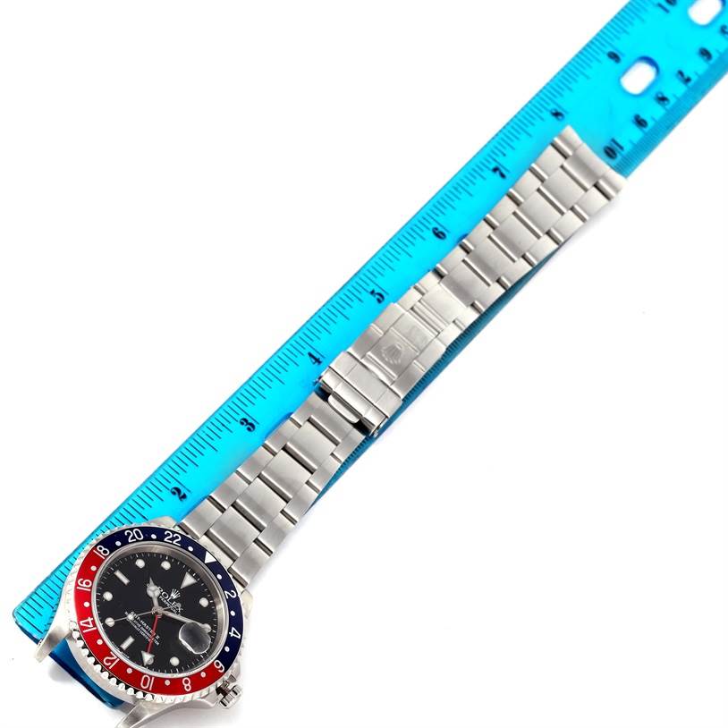 The image shows a Rolex GMT-Master 16710 Men's Stainless Steel Black Dial 16710 Men's Stainless Steel Black Dial watch laid flat beside a blue ruler, highlighting its stainless steel bracelet.