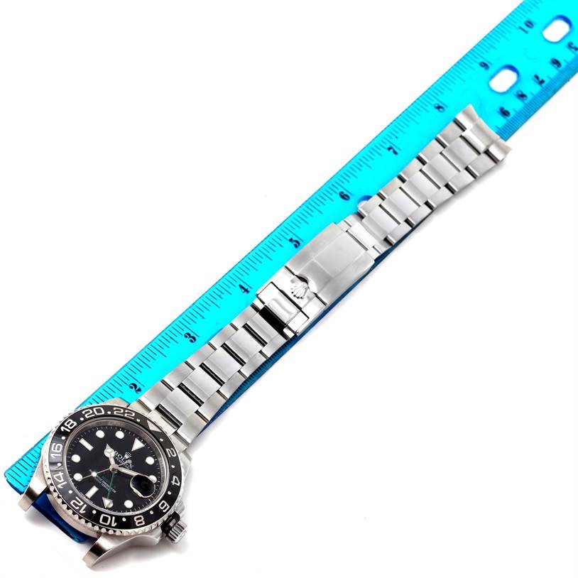 The image shows a top-down view of a Rolex GMT-Master 116710 Men
s Stainless Steel Black Dial 116710 Men
s Stainless Steel Black Dial watch with its bracelet extended and aligned with a blue ruler.