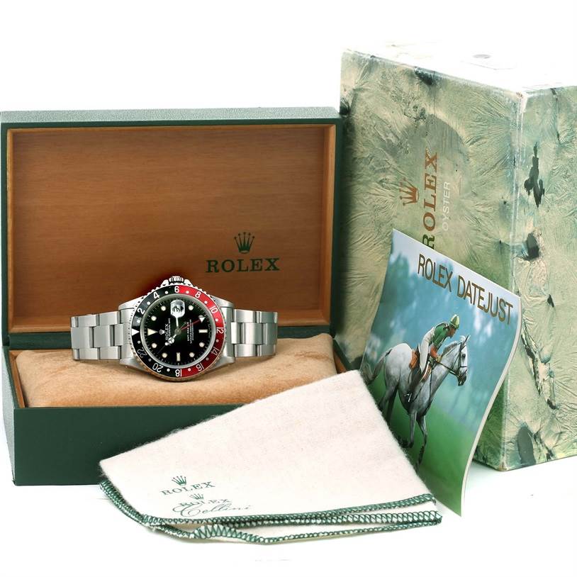 The image shows a front view of a Rolex GMT-Master 16700 Men
s Stainless Steel Black Dial 16700 Men
s Stainless Steel Black Dial watch in its green and wooden box, with a cleaning cloth and booklet beside it.