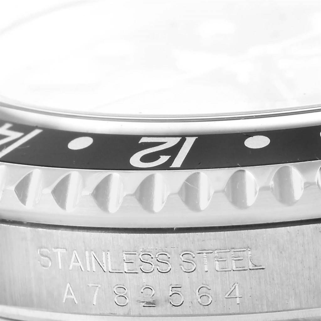 This close-up image of a Rolex GMT-Master 16710 Men's Stainless Steel Black Dial 16710 Men's Stainless Steel Black Dial watch shows part of the bezel with "12" marker and the stainless steel engraved serial number.