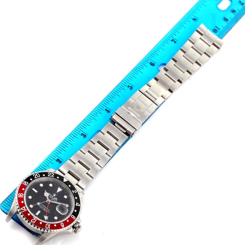The Rolex GMT-Master 16710 Men's Stainless Steel Black Dial 16710 Men's Stainless Steel Black Dial watch is displayed flat with the face on the left and the metal bracelet extended along a blue ruler.
