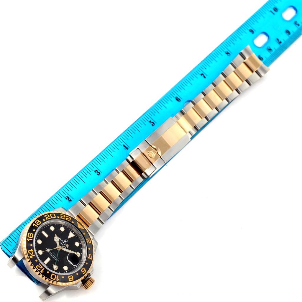 The Rolex GMT-Master 116713 Men's Stainless Steel Black Dial 116713 Men's Stainless Steel Black Dial watch is shown at an angle with the full bracelet extended alongside a blue ruler.