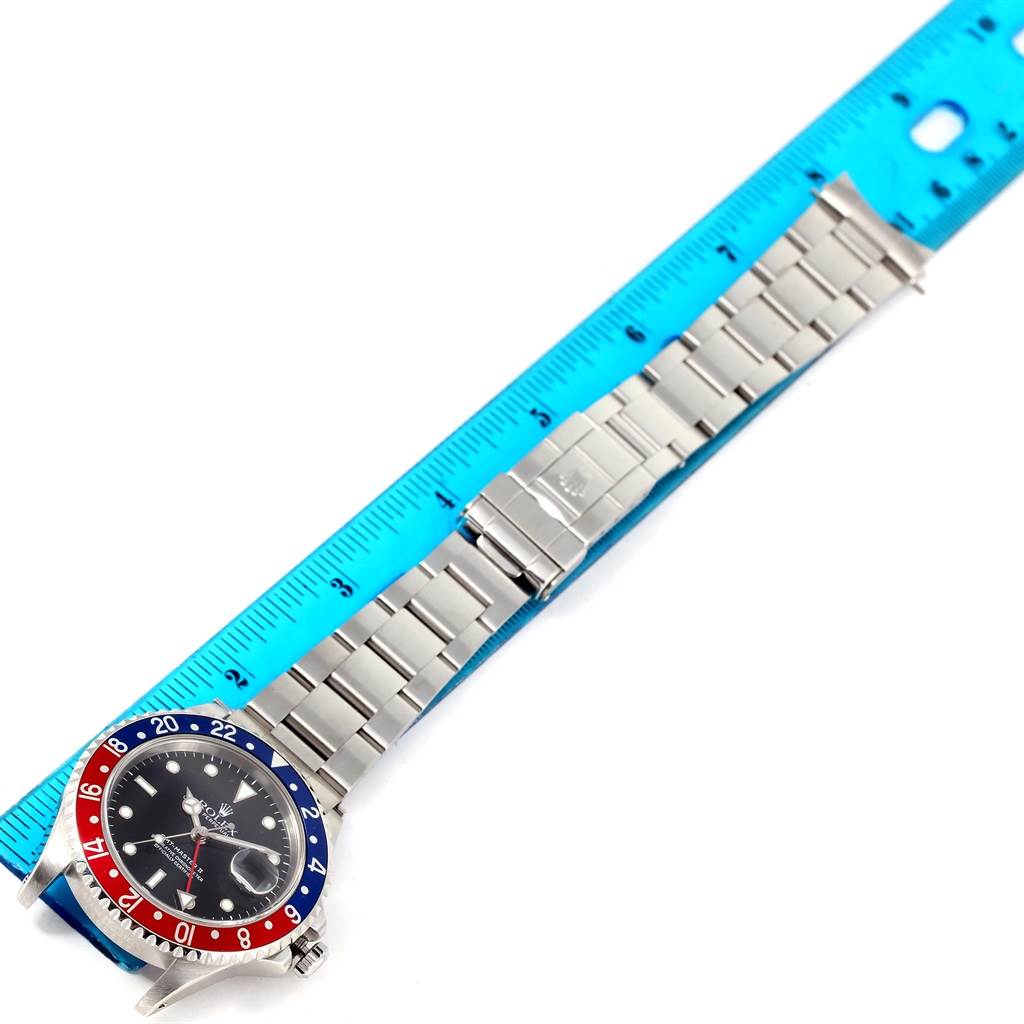 The GMT-Master Rolex watch is shown from a top-down view with its full bracelet and part of its bezel visible alongside a ruler.
