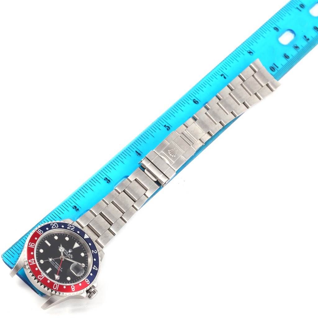 This image shows a Rolex GMT-Master 16710 Men's Stainless Steel Black Dial 16710 Men's Stainless Steel Black Dial watch laid flat with a blue ruler measuring the stainless steel bracelet alongside it.