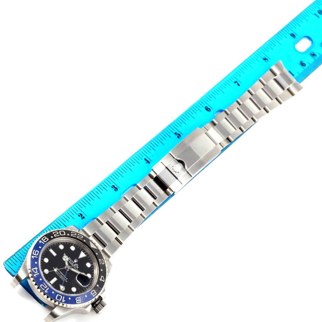 The image shows a top view of a Rolex GMT-Master 116710 Men
s Stainless Steel Black Dial 116710 Men
s Stainless Steel Black Dial watch with a blue/black bezel and its stainless steel bracelet next to a ruler.