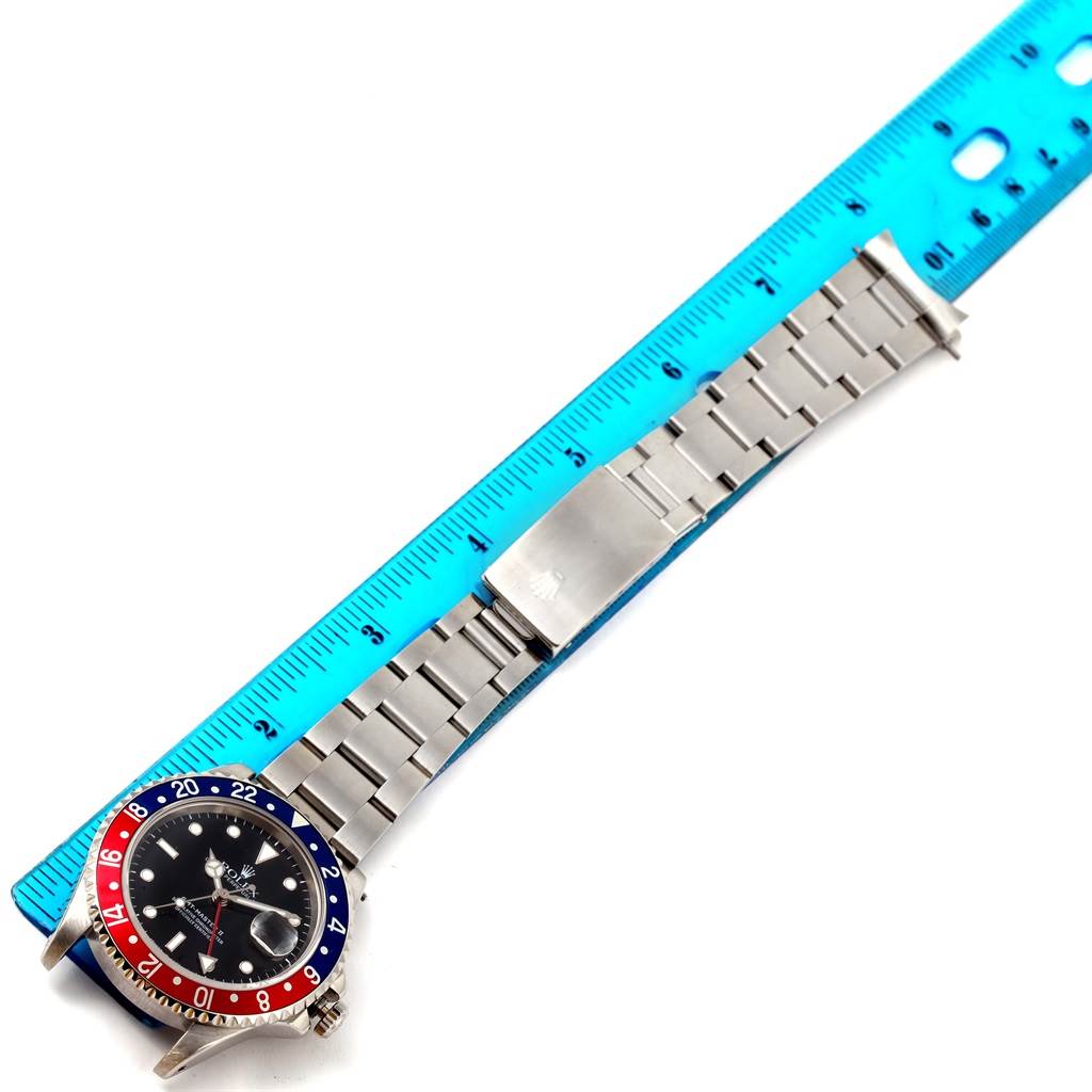 The image shows a Rolex GMT-Master 16710 Men's Stainless Steel Black Dial 16710 Men's Stainless Steel Black Dial watch resting next to a blue ruler, displaying the face and metal bracelet.
