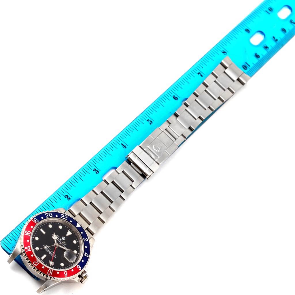 This image shows a top-down view of a Rolex GMT-Master 16710 Men's Stainless Steel Black Dial 16710 Men's Stainless Steel Black Dial watch with the entire bracelet and face visible next to a blue ruler.