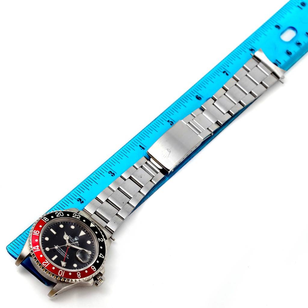 The Rolex GMT-Master 16710 Men
s Stainless Steel Black Dial 16710 Men
s Stainless Steel Black Dial watch is shown from a top-down angle alongside a ruler, displaying the dial and bracelet.