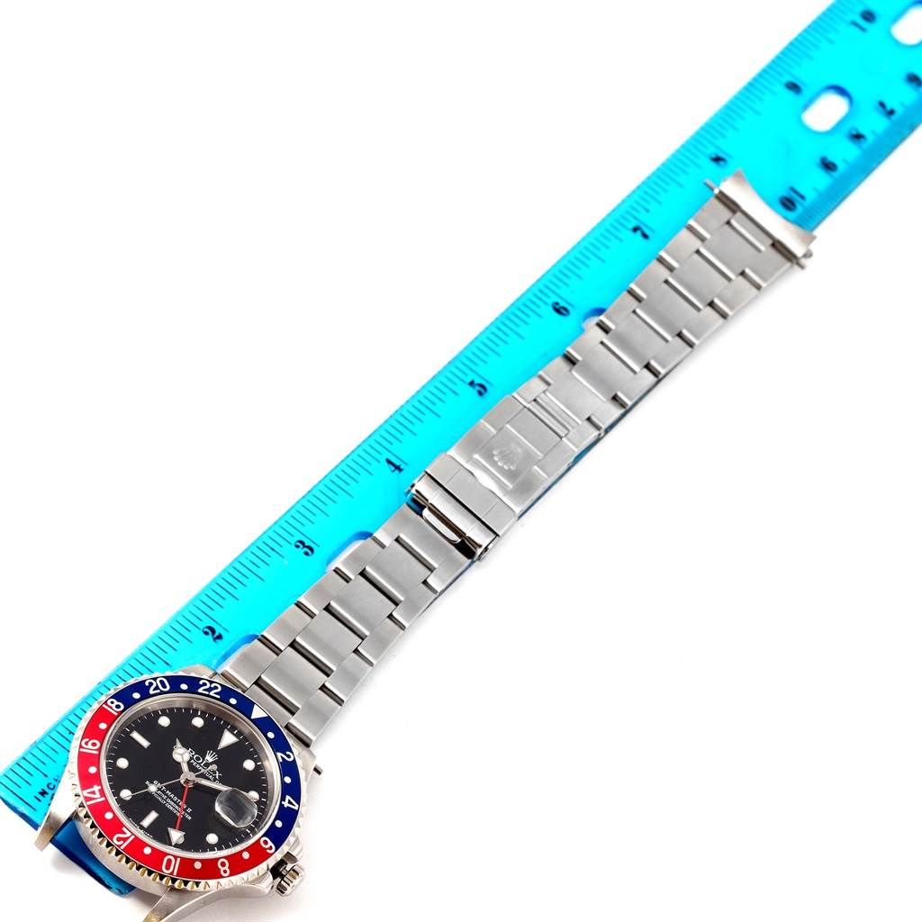 This image shows a Rolex GMT-Master 16710 Men's Stainless Steel Black Dial 16710 Men's Stainless Steel Black Dial watch laid flat next to a blue ruler, displaying the full length of its bracelet and the face at an angle.