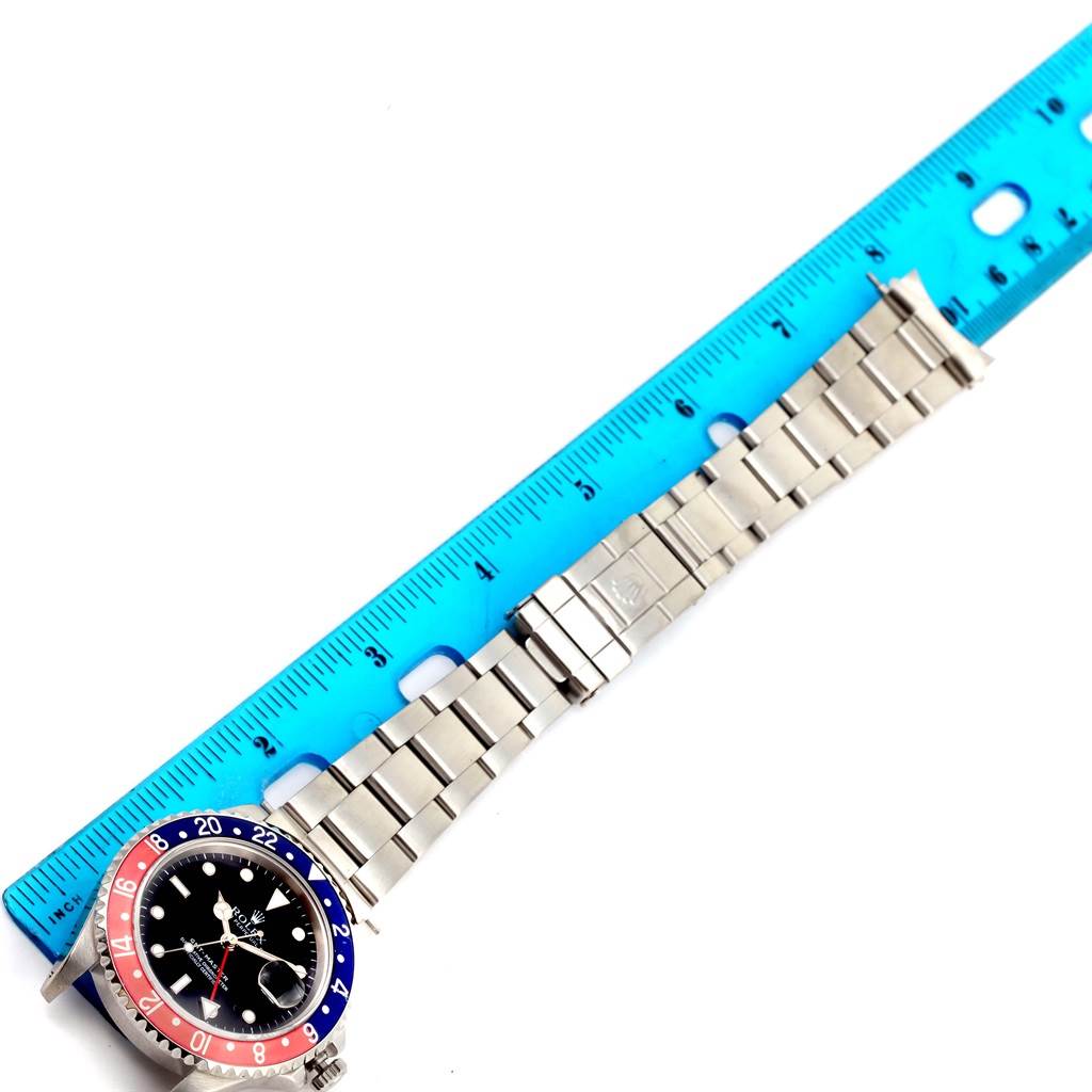 This top-down image shows a Rolex GMT-Master 16700 Men's Stainless Steel Black Dial 16700 Men's Stainless Steel Black Dial watch with a "Pepsi" bezel and metal bracelet beside a blue ruler.