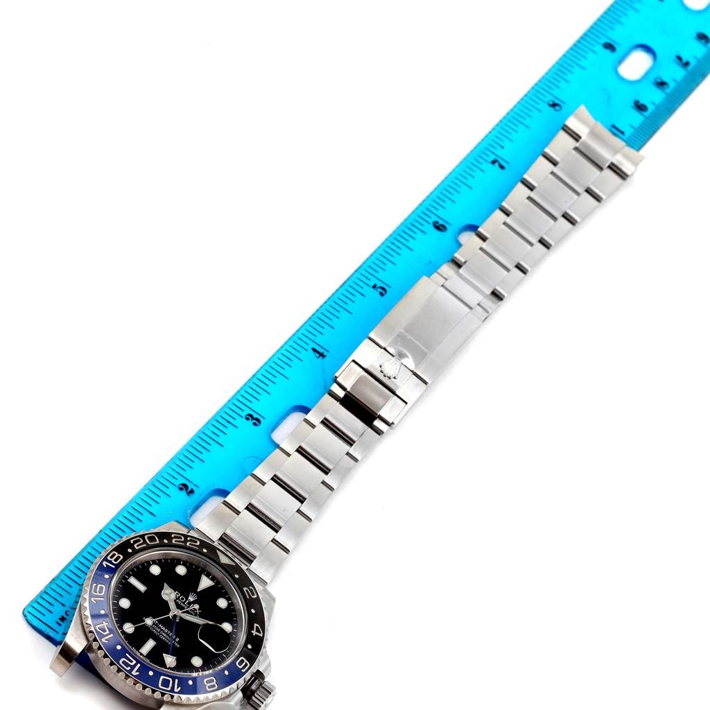 The image shows a top-down view of a Rolex GMT-Master 116710 Men
s Stainless Steel Black Dial 116710 Men
s Stainless Steel Black Dial watch next to a blue ruler, displaying the face and metal bracelet.