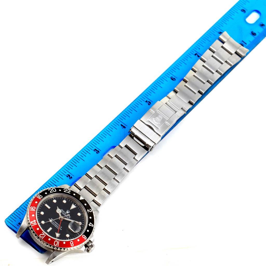 The image shows a top view of a Rolex GMT-Master 16710 Men's Stainless Steel Black Dial 16710 Men's Stainless Steel Black Dial watch, featuring its bezel, dial, and full metal bracelet next to a ruler.