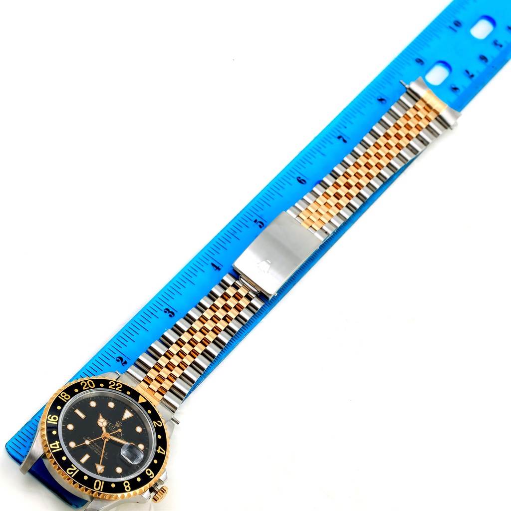 The Rolex GMT-Master 16713 Men's Stainless Steel Black Dial 16713 Men's Stainless Steel Black Dial watch is shown from an overhead angle displaying the dial, bezel, and bracelet, placed adjacent to a blue ruler.