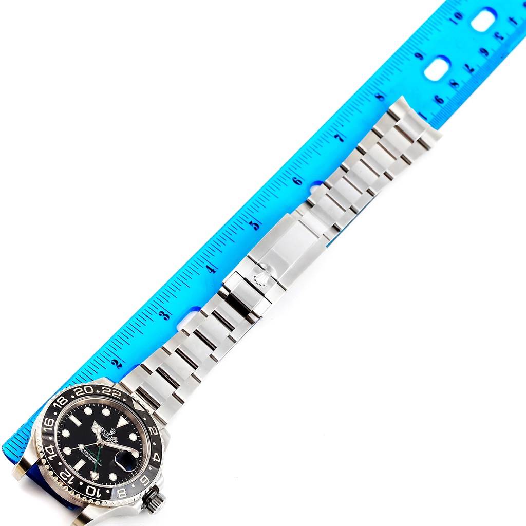 This image shows the Rolex GMT-Master 116710 Men
s Stainless Steel Black Dial 116710 Men
s Stainless Steel Black Dial watch laid flat next to a blue ruler, displaying the watch face, bracelet, and clasp.