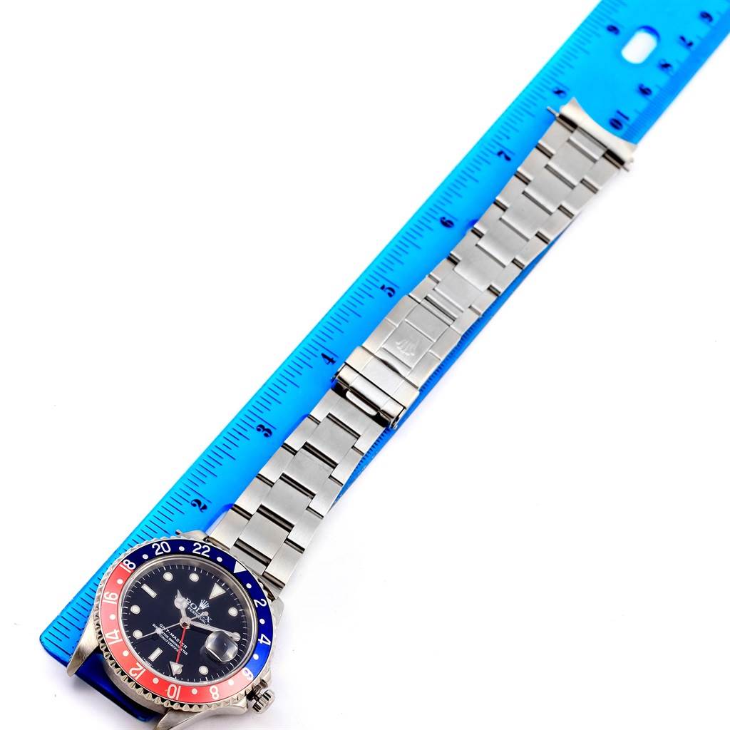 The Rolex GMT-Master 16700 Men's Stainless Steel Black Dial 16700 Men's Stainless Steel Black Dial watch is shown from above, featuring its face, bezel, and bracelet aligned next to a blue ruler.
