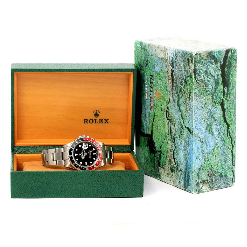 The Rolex GMT-Master 16710 Men's Stainless Steel Black Dial 16710 Men's Stainless Steel Black Dial watch is shown from the front, placed inside its open green and wood-tone box with the outer packaging beside.