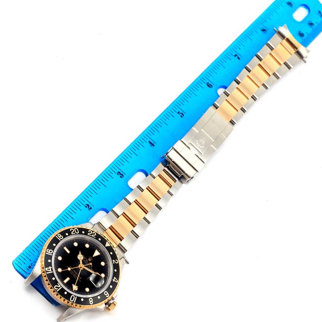 This image shows a Rolex GMT-Master 16713 Men's Stainless Steel Black Dial 16713 Men's Stainless Steel Black Dial watch laid flat with its bracelet extended next to a blue ruler for measurement.