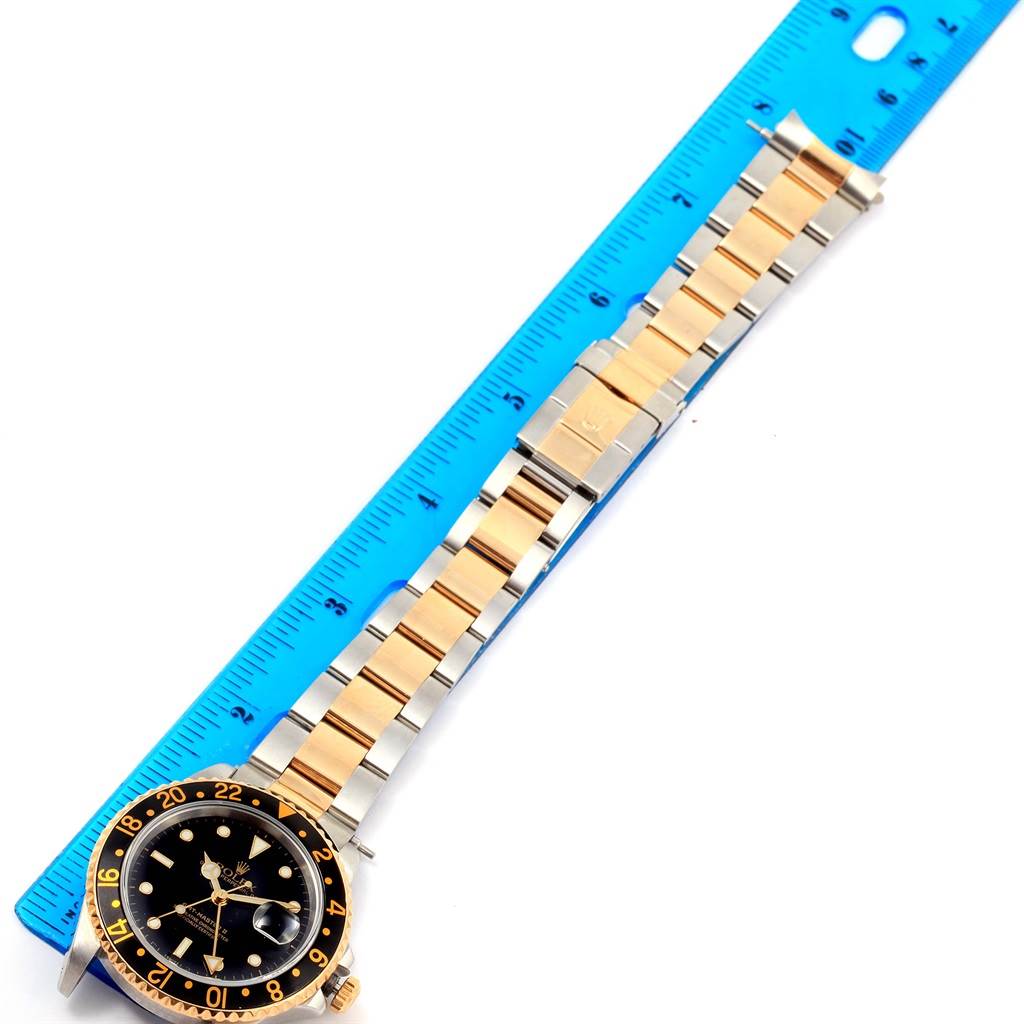 The image shows a Rolex GMT-Master 16713 Men's Stainless Steel Black Dial 16713 Men's Stainless Steel Black Dial watch with a two-tone bracelet and a portion of the watch case, positioned alongside a blue ruler.