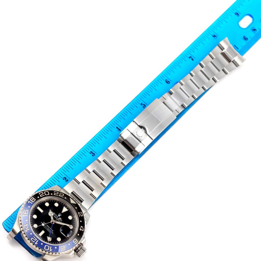 The image shows a Rolex GMT-Master 116710 Men's Stainless Steel Black Dial 116710 Men's Stainless Steel Black Dial watch laid flat with its silver metal strap next to a blue measuring ruler.